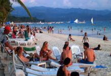 CARIBBEAN-Slight increase in Caribbean tourism arrivals amidst softening demand from North America. Tourists relaxing on a Caribbean beach with cruise ships anchored offshore.