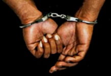 JAMAICA–Police charge a man recently deported from The Bahamas. Jamaican man in handcuffs escorted by police officers at station after being charged following recent deportation from The Bahamas as part of 85-inmate group