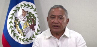 BELIZE-Government announces new measures to deal with the impact of rising oil prices. Belize government official at podium announcing energy measures with oil price chart